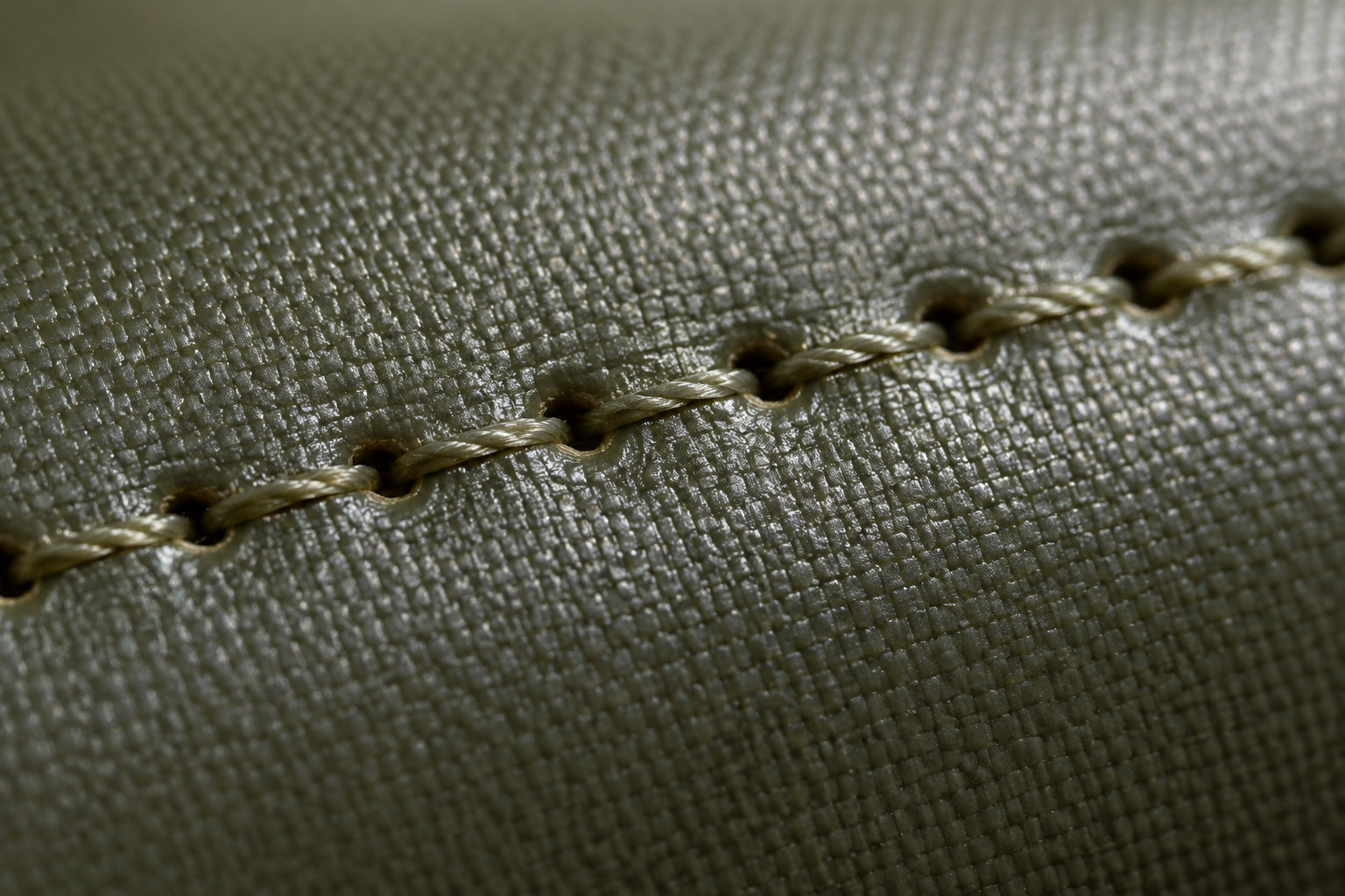 Gros plan sur une couture en fil beige traversant un tissu épais à la texture quadrillée.