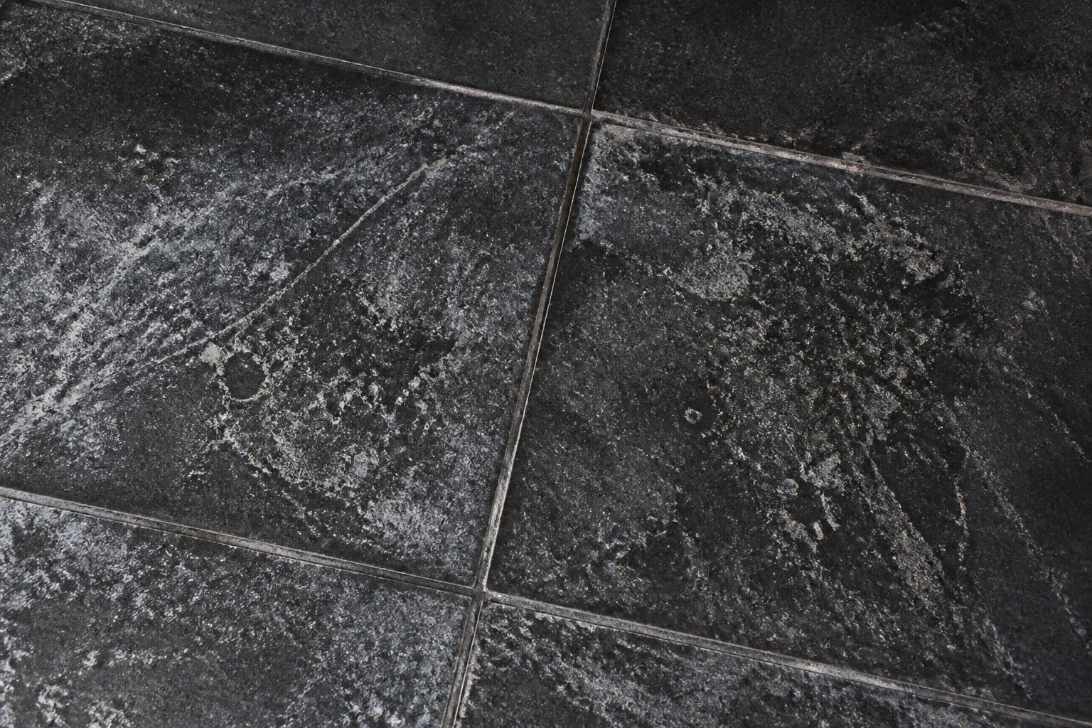 Carrelage noir avec dépôts calcaires blancs visibles en lumière rasante